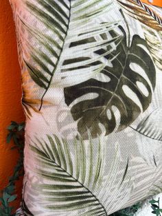 a close up of a pillow with tropical leaves on it and an orange wall in the background