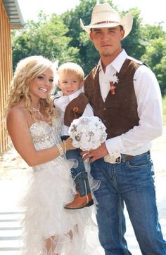 a man in a cowboy hat holding a baby and standing next to a woman wearing a wedding dress