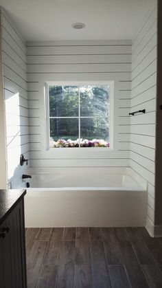 a bathroom with wood flooring and white walls, along with a window that looks out onto the woods