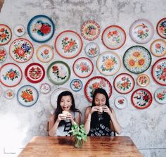 two women sitting at a table with plates on the wall behind them