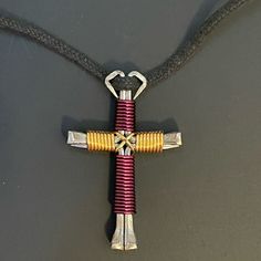 a cross made out of metal and colored cords on a gray surface with a black cord