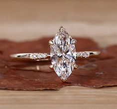 an oval cut diamond engagement ring on top of a wooden surface with leaves around it