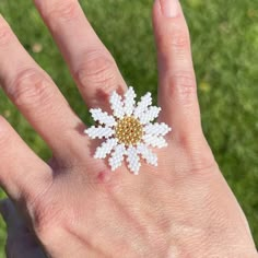 a person's hand with a white and gold flower ring on top of it