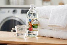 a bottle of water next to a glass on top of a wooden table in front of a washer and dryer