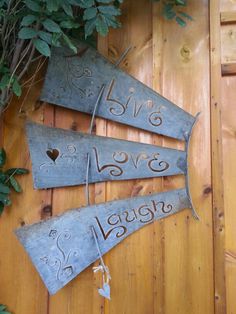 three metal signs that say live laugh love laugh hanging on a wooden wall next to some plants