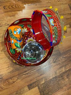 a red bowl sitting on top of a wooden floor next to a glass container with a lid