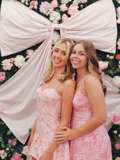 two young women standing next to each other in front of a flower covered wall with pink and white flowers