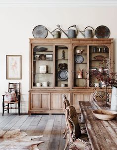 a dining room table and chairs in front of a hutch with dishes on it