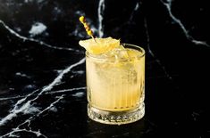 a tall glass filled with lemonade on top of a black marble counter next to an orange slice