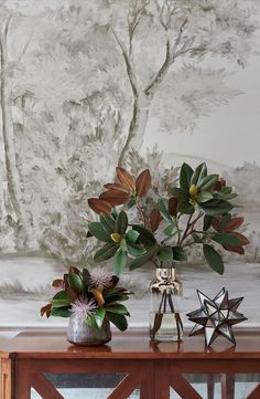 two vases with flowers on a table in front of a wallpapered background