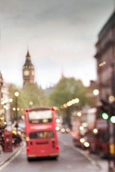 a red double decker bus driving down a street next to tall buildings and traffic lights