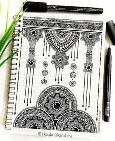 a notebook with black and white designs on it next to some green plants, pencils and markers