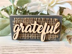 a wooden sign that says grateful sitting on top of a table next to some flowers