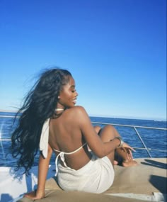 a woman sitting on the back of a boat looking out at the ocean with her long hair blowing in the wind