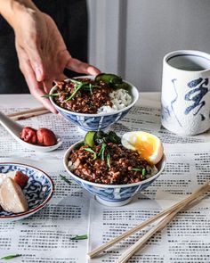 two bowls filled with rice and meat on top of a table next to chopsticks