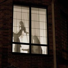 the shadow of a person standing in front of a window with sheer curtains on it