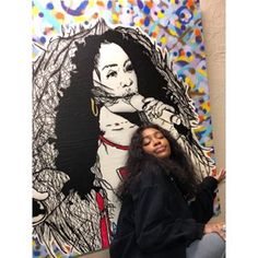 a woman sitting in front of a large painting