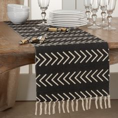 a black and white table runner with tassels on it, next to wine glasses