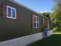 a man is painting the side of a green house with red shutters on it