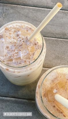 two glasses filled with drinks sitting next to each other on a wooden table and one has a straw sticking out of the top