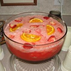 a large bowl filled with ice and fruit on top of a counter next to cups