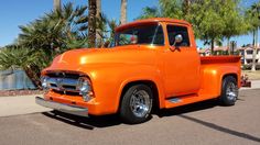 an orange truck is parked on the side of the road near palm trees and water