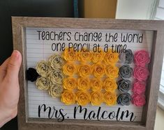 a person holding up a framed sign with flowers on it that says teachers change the world one pencil at a time