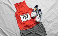 a pair of running shoes next to an orange shirt and gray shorts on a white sheet