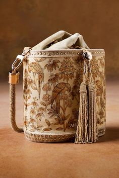 Gold cylindrical shaped bucket bag with Pichhwai, bird, floral hand painted motifs, zari thread embroidery and metallic stud embellishment. Comes with 2 detachable handles. - Aza Fashions Sling Bag Outfit, Boho Handbags, Anita Dongre, Diy Bags Purses, Yarn Bag, Handbag Outfit, Embroidery Bags, Accessories Bags Shoes, Gold Handbags