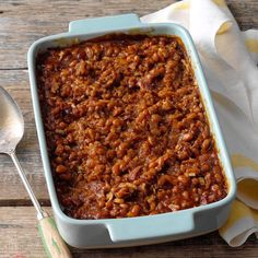 a casserole dish with meat and beans in it on a wooden table next to a spoon