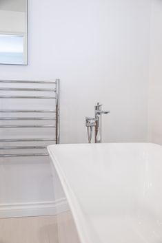 a white bath tub sitting next to a wall mounted towel rack in a bathroom under a mirror