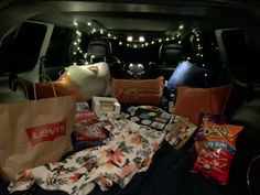 the back of a car filled with lots of items and snacks, including pillows, blankets, and bags