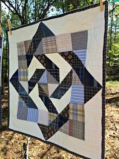 a quilt hanging on a clothes line in the woods with trees and leaves behind it