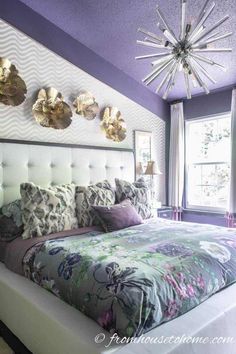 a bedroom with purple walls, white bedding and chandelier above the headboard