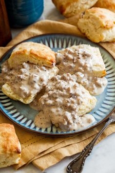 biscuits and gravy on a blue plate with silverware next to it,