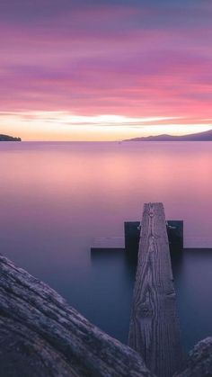 a wooden dock sitting on top of a body of water under a purple sky with clouds