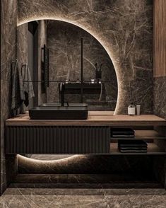 a bathroom with marble walls and flooring is seen in this image, it has a circular mirror over the sink