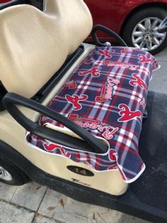 a golf cart with a seat cover on it and a red car in the background