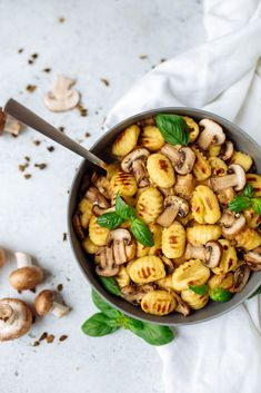 a bowl filled with pasta and mushrooms on top of a white cloth next to some green leaves