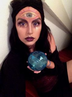 a woman holding a crystal ball with her eyes painted like an eyeball and wearing black clothing