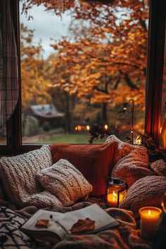 a bed with pillows, blankets and candles on it in front of an open window