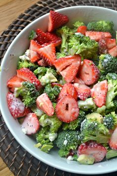 a bowl filled with broccoli and strawberries on top of a wooden table