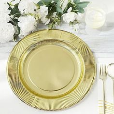 a gold plate sitting on top of a table next to silverware and white flowers