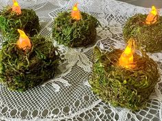 moss covered tea light holders on a lace tablecloth with white doily and small candles in the middle