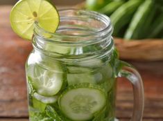 a mason jar filled with sliced cucumbers and limes next to a potted plant