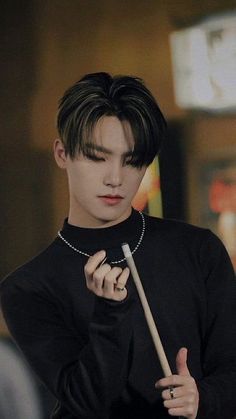 a young man holding a stick in his hand while wearing a black shirt and pearls necklace