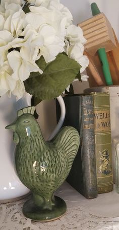 a green vase with white flowers in it sitting on a table next to some books