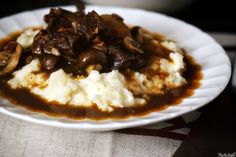 a white plate topped with mashed potatoes covered in mushrooms and gravy on top of a table