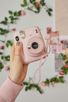 a person holding up a pink camera in front of a wall with flowers on it