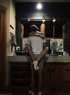 a man sitting on top of a kitchen counter next to a sink under a light